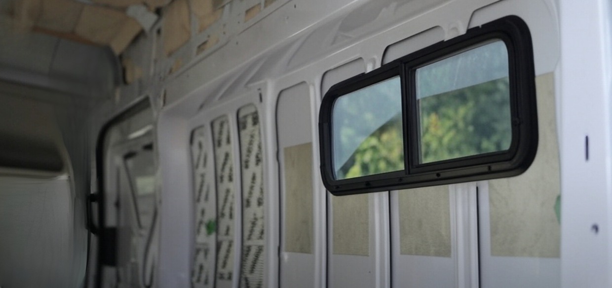 Camper van wall cutout with new window installed and framing started for internal bump-out.