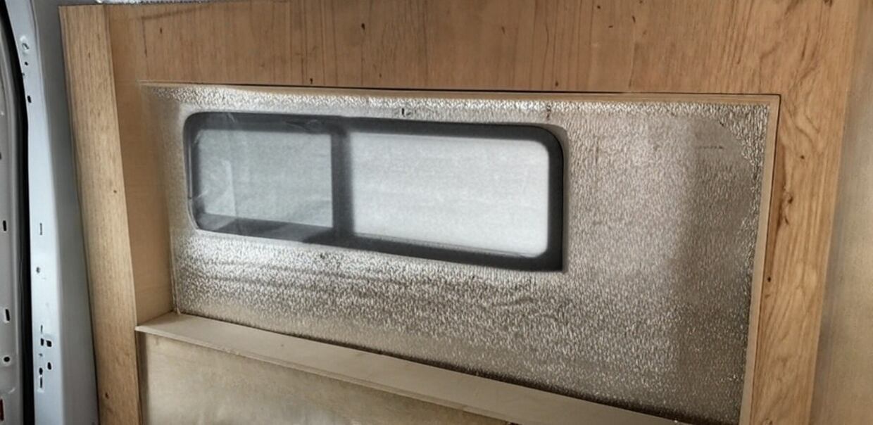 Insulation installed inside framed bump-out section around camper van window.